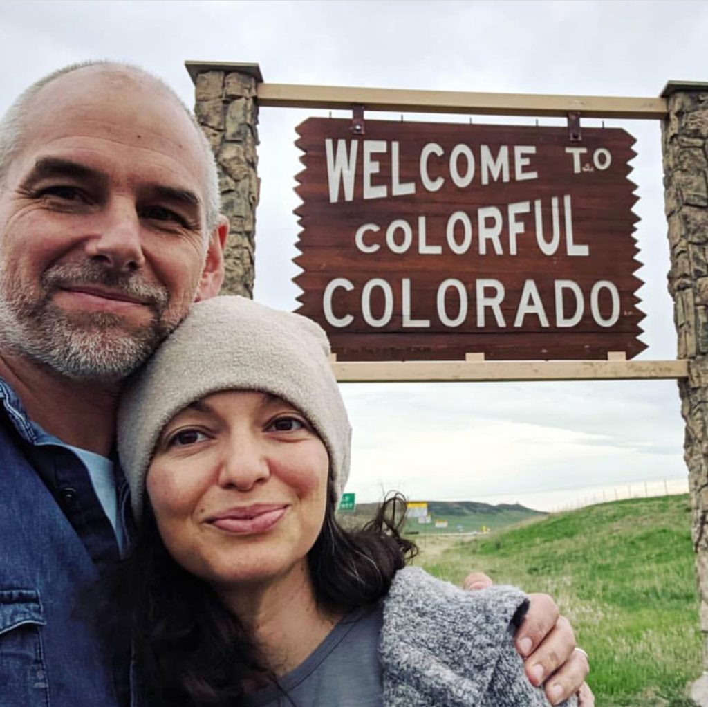 authors Galina & Roland Denzel in front of a "Welcome to Colorful Colorado" sign